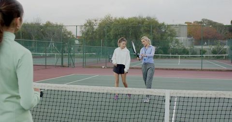 Female tennis coach demonstrating racket technique to young players on outdoor hardcourt