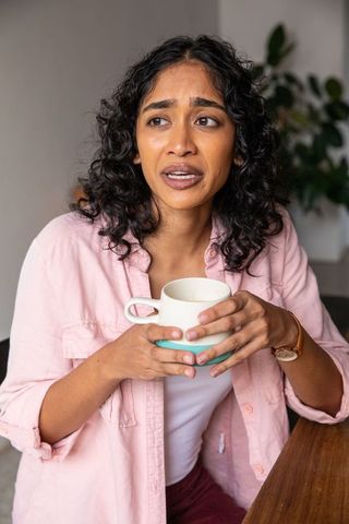 Worried woman holding mug at home in warm living space
