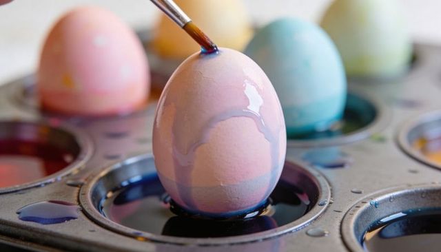 Hand painting pastel easter egg with dripping dye in muffin tin for spring crafts
