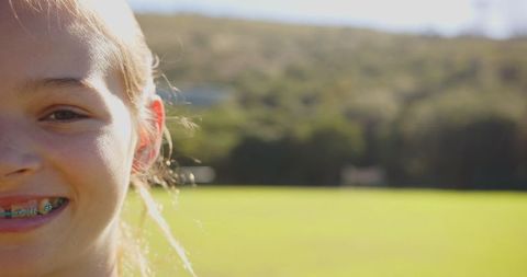 Smiling girl with braces in sunlit field exuding joy and happiness