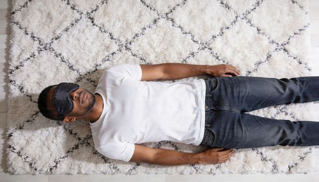 Man lying on shag rug wearing sleep mask relaxing in minimalist home interior for rest