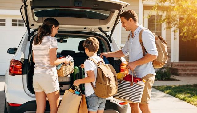 Family packing suv for summer road trip at suburban driveway during golden hour
