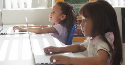 African American girl and classmate using laptops in bright classroom