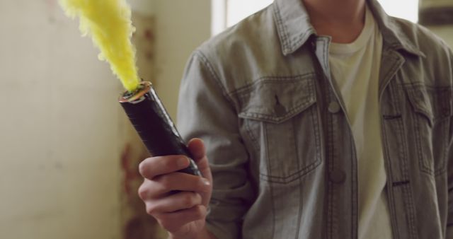 Young biracial man holding a lit smoke flare indoors. The vibrant yellow smoke adds a dynamic element to the scene.