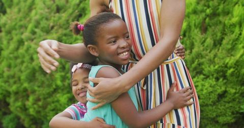 Mother embracing daughters in colorful outfits outdoors