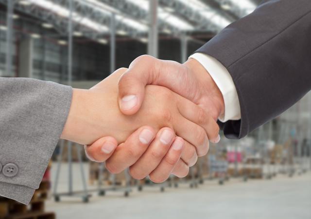 Visualize strong partnerships with professionals shaking hands in a warehouse backdrop. Ideal for highlighting trust, agreements, or successful business transactions in commercial environments.
