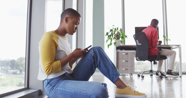 Woman Using Smartphone on Office Floor with Coworker Writing at Desk - Download Free Stock Images Pikwizard.com