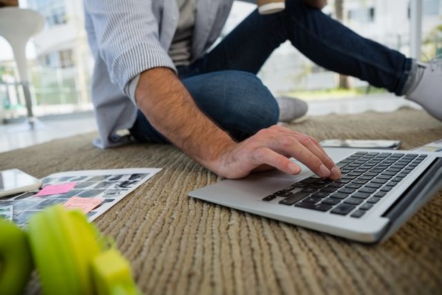 Designer sitting on office floor using laptop, surrounded by design materials. Ideal for illustrating creative work environments, remote work setups, and modern office culture. Suitable for articles on freelance work, productivity tips, and digital design.