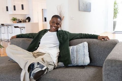 African american man relaxing on modern gray sofa in sunlit minimalist living room