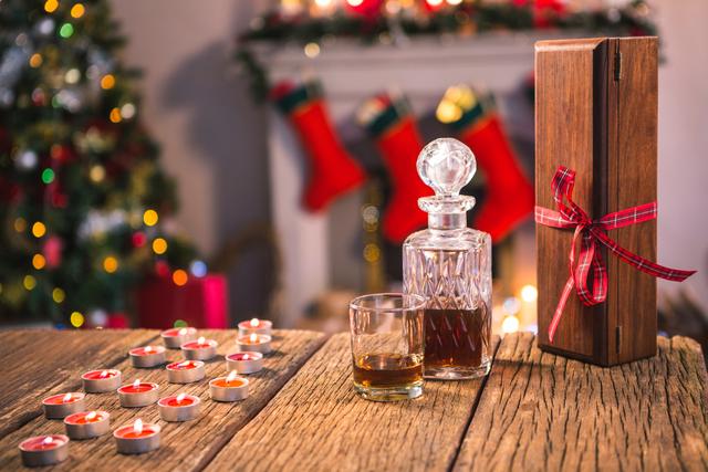 Bottle of whiskey, glass, tealight candle and gift box on wooden table
