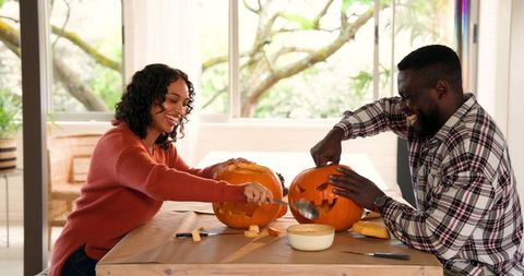 Smiling couple carving pumpkins at bright home table