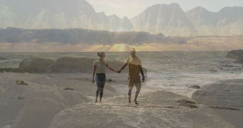 Couple holding hands in front of mountainous seascape at sunset