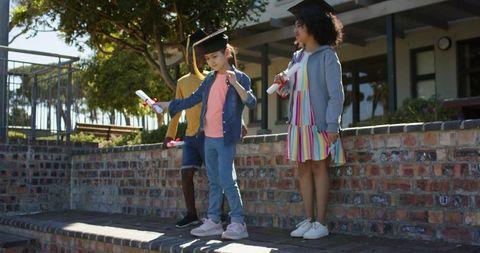 Multiracial children celebrating school graduation holding diplomas and mortarboards