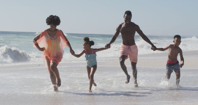 Smiling african american family holding hands and running on sunny beach. healthy, active family beach holiday.
