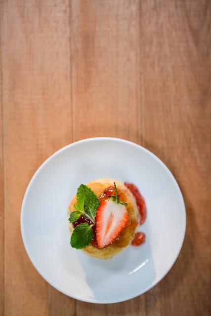This image showcases a beautifully presented gourmet dessert topped with a fresh strawberry and mint leaves, placed on a white plate on a wooden table. Ideal for use in food blogs, culinary websites, restaurant menus, and social media posts promoting desserts or fine dining.