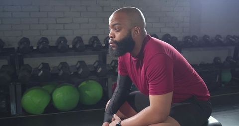 Focused african american man resting on bench in gym preparing for strength workout