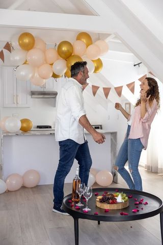 Couple celebrating romantic loft party with balloons, wine, charcuterie and rose petals