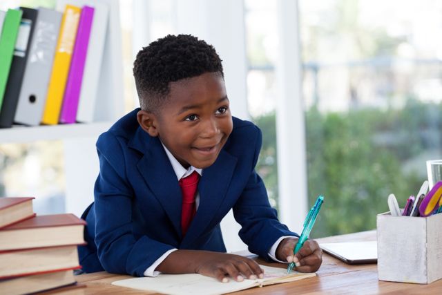 Young boy in a suit writing at a desk in an office. He is smiling and appears engaged. Ideal for concepts related to education, business, ambition, and future leaders. Suitable for use in educational materials, business promotions, and inspirational content.