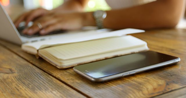 Close-up of smartphone, notepad, and person using laptop on wooden desk - Download Free Stock Images Pikwizard.com