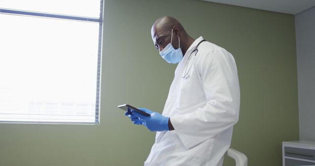 Doctor in a white coat and wearing a surgical mask using a digital tablet in a modern medical office. Ideal for healthcare, medical technology, hospital brochures, advertisements promoting healthcare services, and telemedicine applications.