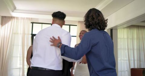 African american friends greeting in living room with sheer curtains, home gathering