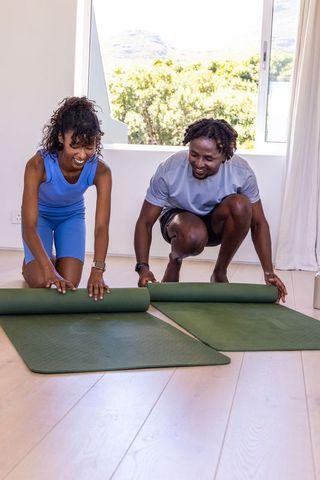 African american couple rolling out yoga mats for home workout and partner fitness routine