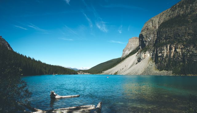 Beautiful serene mountain lake with clear blue water surrounded by high cliffs and evergreen trees under a clear sky. An ideal image for travel brochures, nature magazines, and outdoor adventure marketing materials.