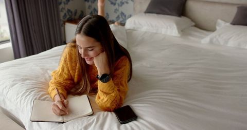 Young woman writing journal on bed in cozy bedroom
