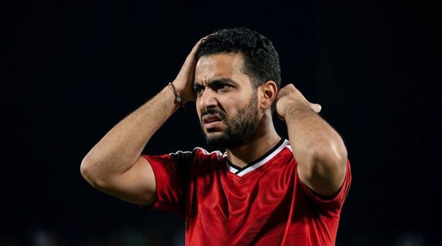 Clutching head in frustration male soccer player wearing red jersey at night stadium