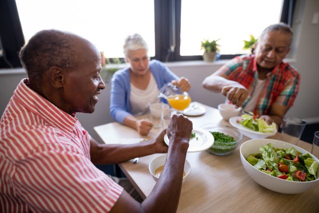 Senior people having juice and salad while sitting at table in nursing home