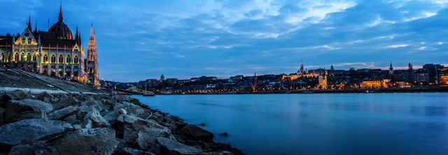 Panoramic view of Budapest's iconic cityscape at twilight, reflecting in the Danube River. Illuminated historic buildings and landmarks create a picturesque scene, making it ideal for travel promotions, city guides, and tourism marketing materials.