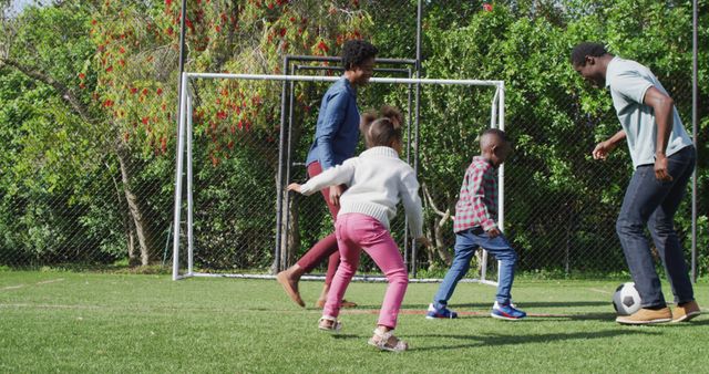 Happy african american family playing football in park. Spending quality time with family outdoors concept.