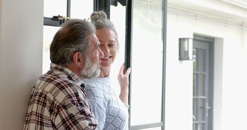 Happy senior couple enjoying conversation by glass door