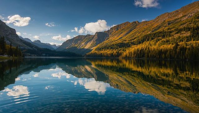 Panoramic autumn mountains reflecting in crystal alpine lake, cloud mirror and blue sky