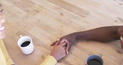 Interracial Couple Holding Hands Over Coffee at Wooden Table