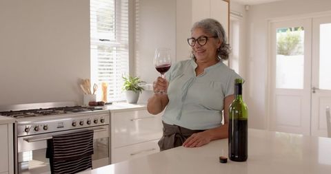 Elderly Woman Savoring Red Wine in Modern Kitchen
