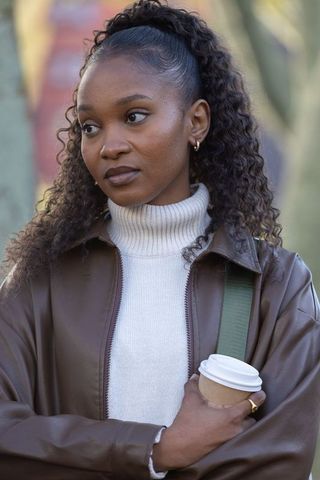 Thoughtful woman holding coffee in brown leather jacket and cream turtleneck