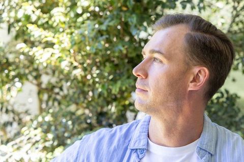 Sunlit contemplative man gazing upward in garden headshot for wellness lifestyle branding