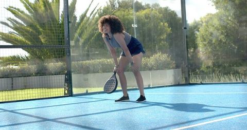 African woman smiling while holding paddle racket on blue padel court in sunshine