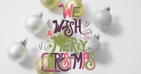 Hand-lettered merry christmas greeting over silver and gold baubles flatlay high-key