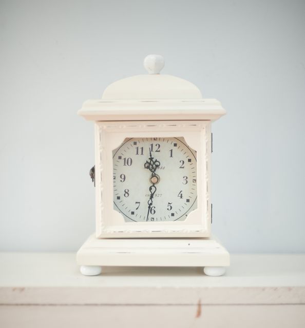 Vintage white table clock with an intricate design and classic appeal. Clock features clear numbering and a rustic finish, ideal for home decor, antique-themed spaces, and evoking a nostalgic atmosphere. Use it in advertisements for interior design products, lifestyle blogs, or time-related concepts.