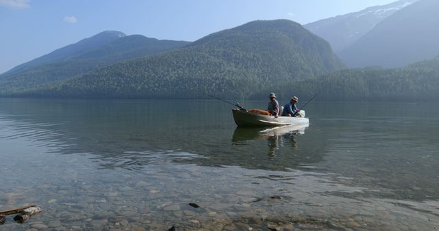 Men fishing from boat on clear lake surrounded by mountains. Use for nature, outdoor activities, leisure time content.