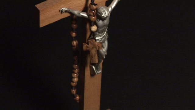 Wooden cross with a crucifix and rosary beads hanging on a dark background represents religious observance and devotion. Ideal for use in religious content, articles about Christianity, or discussions about faith and spirituality. Suitable for spiritual or church newsletters and educational materials.