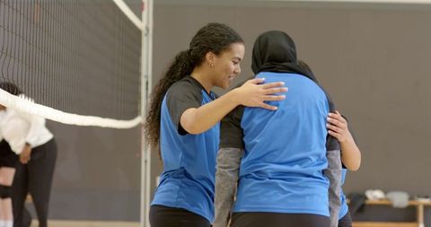 Diverse female volleyball teammates hugging and encouraging after point on indoor court