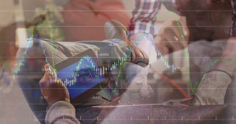 Relaxing on couch holding tablet while partner using pliers, financial market chart overlay