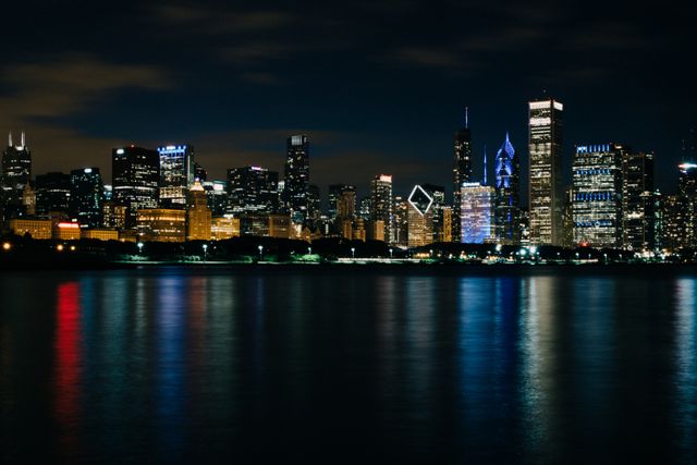 Nighttime cityscape of Chicago with lit up buildings reflecting on still water. Ideal for travel-related content, urban lifestyle blogs, real estate marketing, city tourism advertisements, or business presentations focusing on urban life.