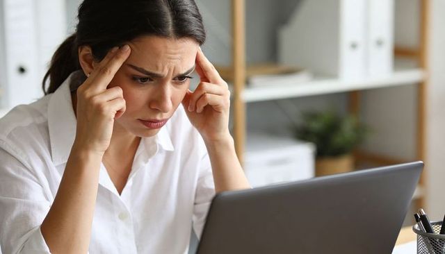 Woman pressing temples while focusing on laptop, stressed professional at desk