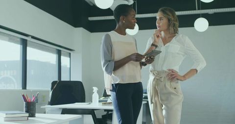 Professional women in office discussing project on tablet