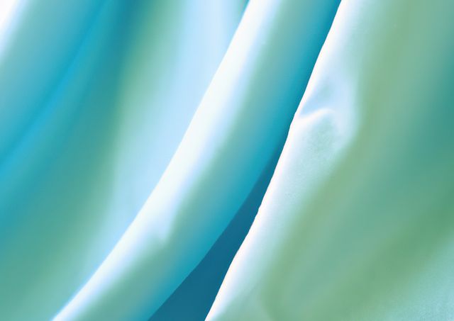 Smooth blue fabric texture with soft, flowing curves, creating a calming and serene atmosphere. Use as background for fashion design, websites, graphic design projects, or advertising materials. Ideal for presentations emphasizing softness, elegance, or luxury.