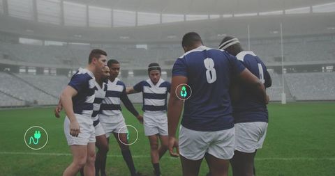 Rugby team huddling on misty stadium pitch wearing navy kit showing number 8 and icons